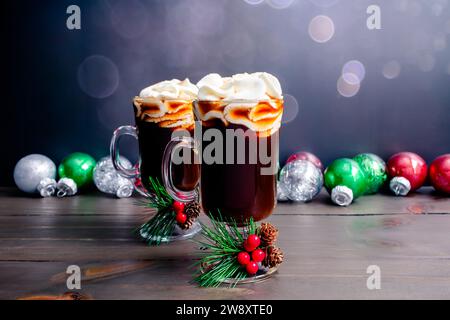 Gewürzter Weihnachtskaffee mit Schlagsahne: Zwei Glasbecher frisch gebrühten Gewürzkaffee mit Weihnachtsschmuck im Hintergrund Stockfoto