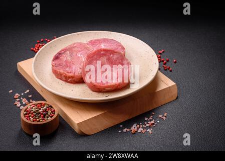 Rund geformte Steaks von rohen, saftigen Thunfisch mit Salz und Gewürzen auf dunklem Betonhintergrund Stockfoto