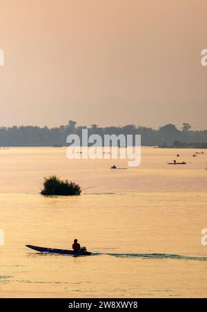 Am frühen Abend schweben Flussboote über das ruhige Wasser des Mekong, im Si Phan Don Archipel, durch Strahlen von warmem goldenem Licht, das von t reflektiert wird Stockfoto