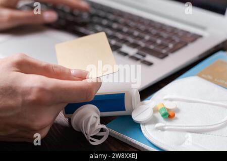 Abbildung: Laptop, Bank-Goldkarte, Pillen und Coronavirus-Schutzausrüstung. Krankenversicherungskonzept. Das Arzneimittel. Gemischte Medien Stockfoto