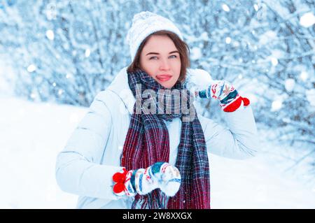 Porträt eines schönen Mädchens, das einen Schneeball wirft. Konzept für Weihnachtsferien, Winterspiele, Glück und Spaß. Gemischte Medien Stockfoto