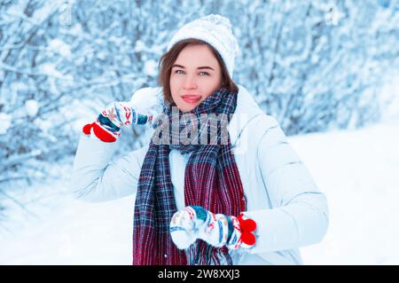 Porträt eines schönen Mädchens, das einen Schneeball wirft. Konzept für Weihnachtsferien, Winterspiele, Glück und Spaß. Gemischte Medien Stockfoto