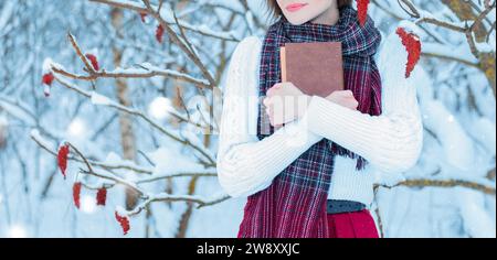 Kein Namensporträt eines charmanten Mädchens, das ein Buch im Winterwald umarmt. Konzept von Weihnachten, Winterfeiern, Spaziergängen in den Wäldern, Urlaub. Stockfoto