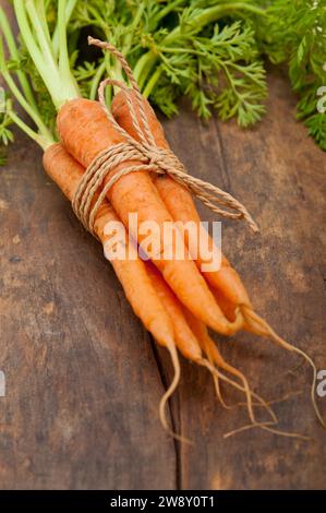 Frische BabyKarotten mit Seil auf einem rustikalen Tisch, Lebensmittelfotografie Stockfoto