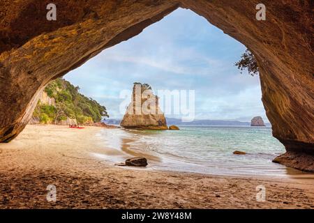 Blick von einer Höhle auf einen Sandstrand und einen einsamen Felsvorsprung im Meer, Cathedral Grove, Coromandel, Neuseeland Stockfoto