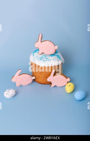 Drei süße pinkfarbene Lebkuchen in Form eines Kaninchens auf Osterkuchen und dekorative Eier Stockfoto