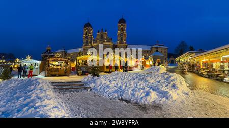 Einsiedeln, Schweiz - 5. Dezember 2023: Weihnachtsmarkt vor der Benediktinerabtei Einsiedeln mit seiner mächtigen Basilika in blauer Stunde Stockfoto