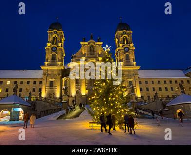 Einsiedeln, Schweiz - 5. Dezember 2023: Weihnachtsbaum vor der Benediktinerabtei Einsiedeln mit seiner mächtigen Basilika in blauer Stunde Stockfoto