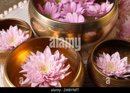 Tibetische Klangschalen mit Wasser und schönen Blumen auf dem Tisch, Nahaufnahme Stockfoto