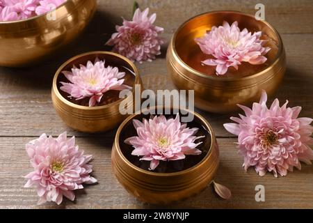 Tibetische Klangschalen mit Wasser und wunderschönen Blumen auf Holztisch Stockfoto
