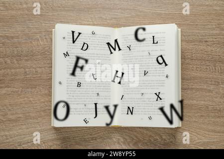 Offenes Buch mit Buchstaben, die auf hölzernem Hintergrund herausfliegen, Draufsicht Stockfoto
