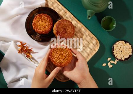 Hände einer Frau, die Mondkuchen auf Tee-Tisch-Hintergrund hält. Werbeszene von Mondkuchen - ein traditioneller Kuchen während des Mid-Herbstfestes in Asien Stockfoto