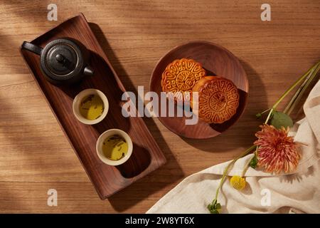 Hintergrund des traditionellen chinesischen Festivals Mitte Herbst mit Mondkuchen, Tee auf Holztabletts und schöner Blume auf weißem Tuch. Foto im chinesischen Stil Stockfoto