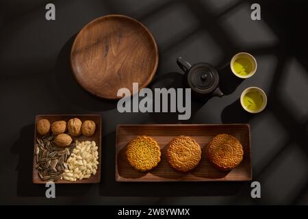 Blick von oben auf Holztabletts mit Mooncakes und verschiedenen Samen auf schwarzem Hintergrund. Chinesisches Mid-Herbstfestival-Konzept. Werbefot Stockfoto