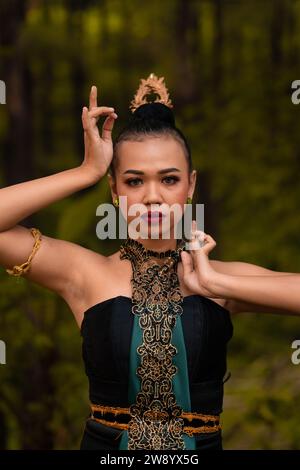 Tapferes Gesicht einer asiatischen Frau in einem traditionellen grünen Kostüm mit goldenen Accessoires am Körper während des Wettkampfes bei einem Tanzfestival vor der Tür Stockfoto