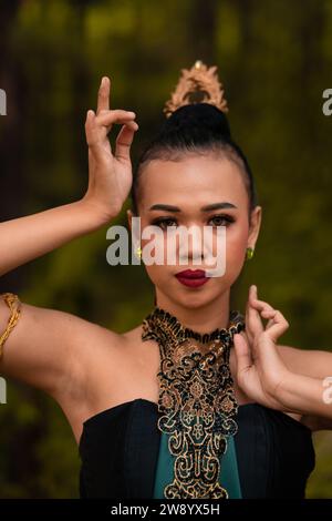 Tapferes Gesicht einer asiatischen Frau in einem traditionellen grünen Kostüm mit goldenen Accessoires am Körper während des Wettkampfes bei einem Tanzfestival vor der Tür Stockfoto