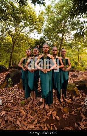 Eine große Aufnahme einer asiatischen Frau, die zusammen im Wald steht, während sie ein grünes Tanzkostüm mit toten Blättern im Hintergrund trägt Stockfoto