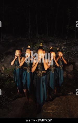 Eine Gruppe indonesischer Frauen, die eine braune Holzmaske in einem grünen Rock zwischen dem Felsen im Wald tragen Stockfoto