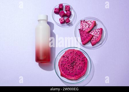 Blick von oben auf eine Glasflasche, die mit frischen Scheiben roter Drachenfrucht auf lila Hintergrund dekoriert ist. Der hohe Vitamin-B3-Gehalt in Drachenfrüchten beruhigt Stockfoto