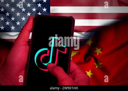 Die Hände schließen sich. Diese Abbildung zeigt das tiktok-Logo auf dem Bildschirm eines Mobiltelefons. Vor dem Hintergrund der Satinwellen des Amerikaners und CH Stockfoto