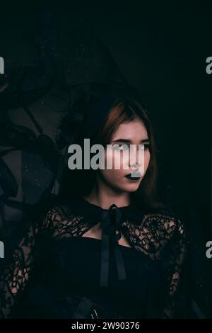 Ein asiatischer Teenager hat ein unheimliches Aussehen mit schwarzem Make-up und einem schwarzen Kleid wie eine Hexe vor Halloween in der Nacht Stockfoto