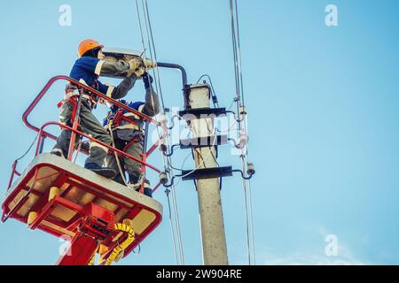 Zwei Elektriker von der Halterung der Antennenplattform oder des Krans reparieren die Straßenbeleuchtung. Professionelle Elektriker tragen Helme, Overalls und Versicherungsarbeiten in der Höhe. Ansicht der Arbeiter von unten nach oben zum Himmel. Authentischer Workflow. Stockfoto