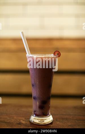 Ein Nahfoto eines Glases lila Flüssigkeit, wahrscheinlich Traubensaft, mit einer einzigen grünen Traube darüber. Das Glas sitzt auf einem dunklen Holztisch, und Stockfoto