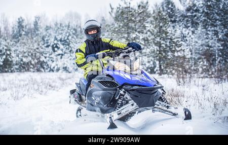 Der Mensch fährt Schneemobil in den Bergen. Pilot auf einem Sportschneemobil in einem Bergwald. Sportler fährt ein Schneemobil in den Bergen. Schneemobil in Stockfoto