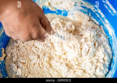 Frau, die Teig mit Hefeteig kneten. Teig zubereiten, Zutaten mischen. Frau rührt sich um Löffel in Schüssel Mehl. Sauerteig von Grund auf herstellen Stockfoto
