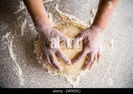 Kochen mit Liebe. Weibliche Hände, die den Teig in Herzform halten. Berühren Sie den rohen Teig sanft mit den Händen in Form eines Herzens. Weibliche Hände, die Teig halten Stockfoto