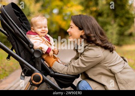 Junge Frau mit einem süßen Mädchen im Kinderwagen im Herbstpark Stockfoto