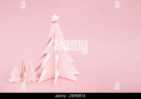 Rosafarbene Origami-Weihnachtsbäume. Einfarbiger Hintergrund für Winterferien. Stockfoto