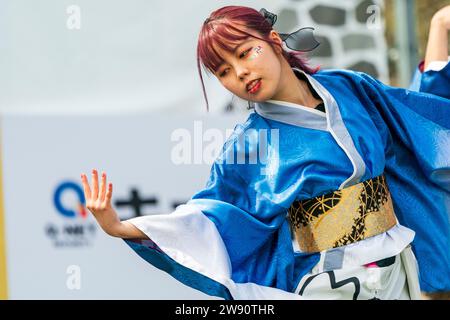 Die junge japanische yosakoi-Tänzerin tanzt an der Seite des Bildes und lehnt sich in die andere Seite mit ausgestreckter Hand und Fingern. Trägt blaue Yukata. Stockfoto