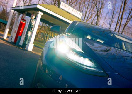 Warren Center, PA, USA - 22. Dezember 2023: Ein blaues Tesla Model 3, ein Elektrofahrzeug, wird in der Nähe einer alten Tankstelle in einer ländlichen Stadt fotografiert. Stockfoto