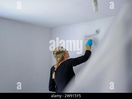 Rückansicht einer Frau, die die Wand ihrer Wohnung mit einer großen Malerwalze in ihrer neuen Wohnung malte Stockfoto