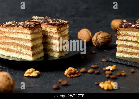 Ein Stück Dobosh-Kuchen. Ungarischer Biskuitkuchen mit Schokoladenbuttercreme und Walnüssen. Dunkler Hintergrund Stockfoto