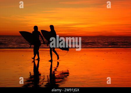Zwei Teenager-Surfer, die in einer Silhouette vom Sonnenuntergang sehen, verlassen das Meer mit ihren Surfbrettern nach einem Tag am Strand in Kalifornien Stockfoto