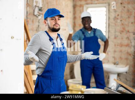 Vorarbeiter schreit nach dem verwirrten Arbeiter auf der Baustelle Stockfoto