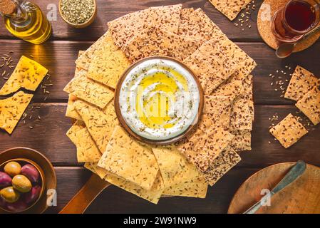 Sammlung köstlicher gesunder Cracker mit frischen Kräutern oben. Serviert mit cremigem Dip, eingelegten Oliven und einer Tasse Tee. Stockfoto