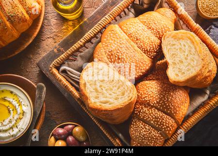 Köstliches frisches Backcroissant mit Sesamsamen und Thymian in einem kleinen Holzkorb. Serviert mit cremigem Käsedip und eingelegten Oliven. Stockfoto