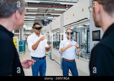 Kollegen beobachten zwei Techniker, die Augmented-Reality-Brillen in einer Fabrik tragen Stockfoto