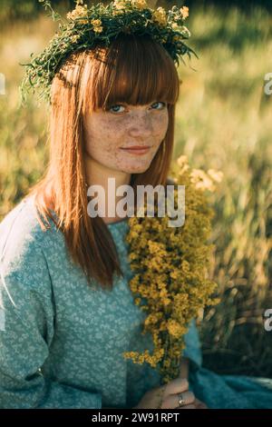 Junge Rothaarige Frau, die einen Blumenkranz auf dem Feld trägt Stockfoto