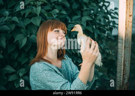 Lächelnde junge rothaarige Frau mit Sommersprossen, die auf Entlein blickt Stockfoto