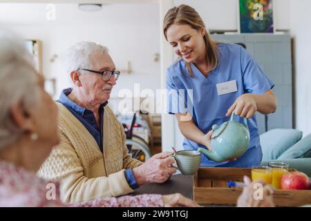 Lächelnder Arzt serviert Tee für Seniorenpaare, die am Tisch sitzen Stockfoto