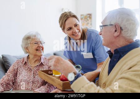 Glücklicher Mitarbeiter im Gesundheitswesen servieren Saft und Essen für Seniorenpaare zu Hause Stockfoto