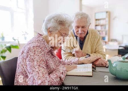 Senior-Mann mit Frau, die Buch liest und Hände am Tisch hält Stockfoto