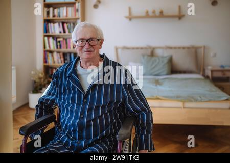 Lächelnder Seniorenmann, der zu Hause im Rollstuhl sitzt Stockfoto