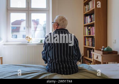 Besinnlicher Seniorenmann, der zu Hause auf dem Bett sitzt Stockfoto