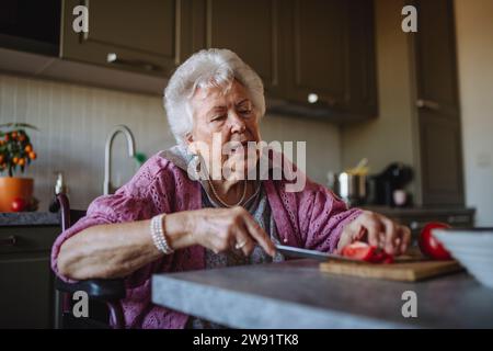 Senior Frau schneidet Tomaten am Tisch in der Küche Stockfoto