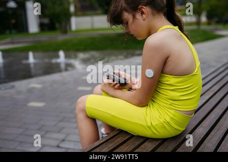 Ein Mädchen mit Diabetes überprüft ihren Blutzuckerspiegel an einer Insulinpumpe, trägt einen CGM-Sensor Stockfoto